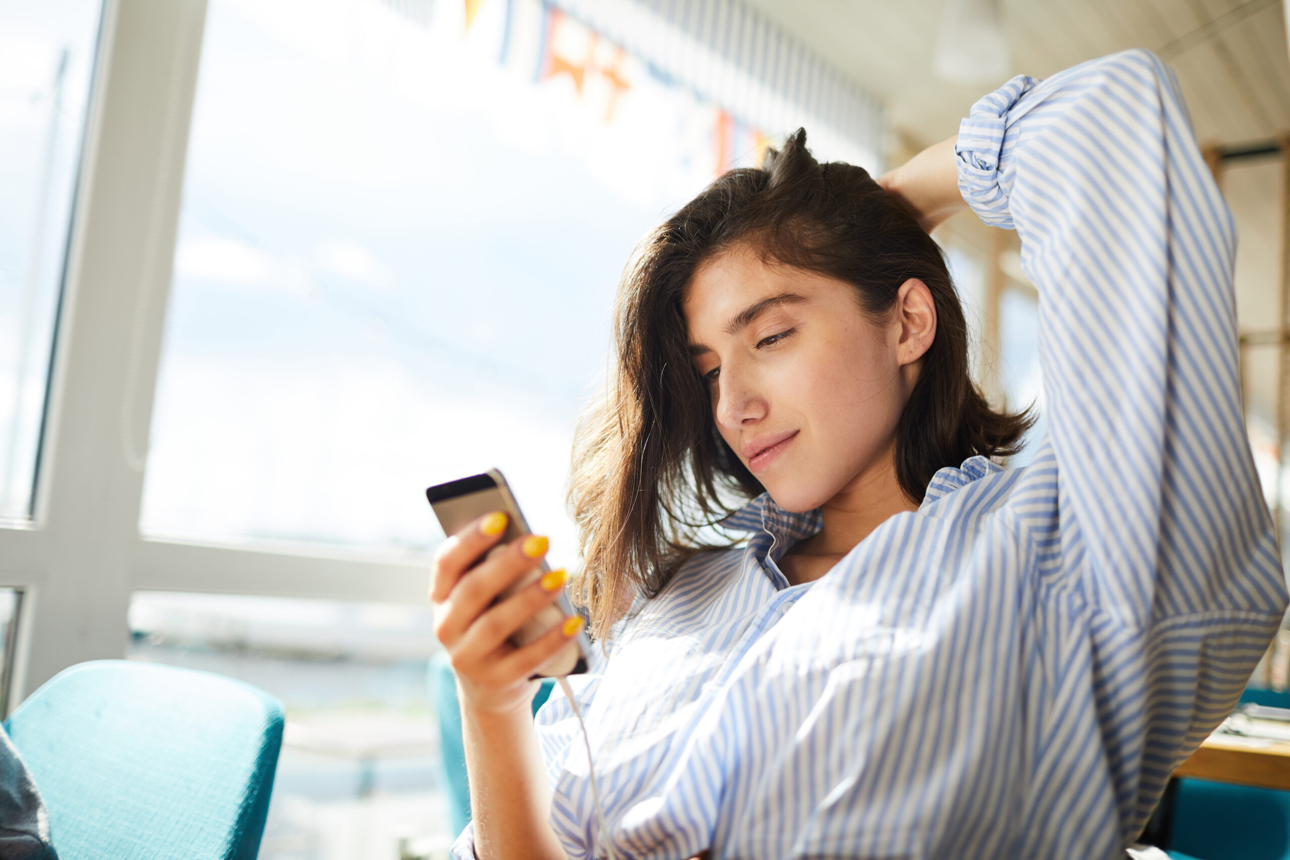 Young relaxed woman in casual shirt reading message from her boyfriend in cafe