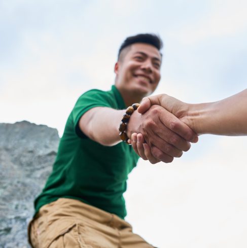 Smiling Asian man helping hiker to climb the mountain