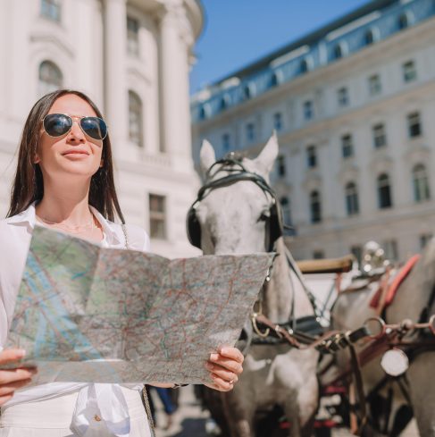 Happy young woman with a city map in old streets. Travel tourist girl with map in Vienna outdoors during holidays in Europe.